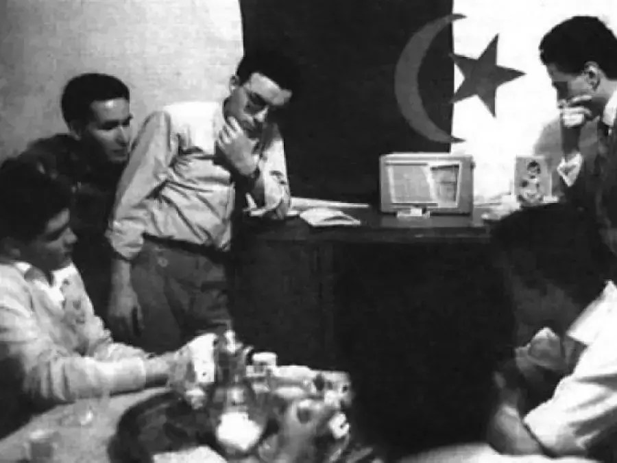 black and white image of five men gathered around a radio receiver, listening intently.
