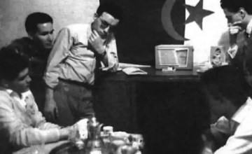 black and white image of five men gathered around a radio receiver, listening intently.